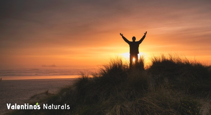 Man standing on a hill with his arms out wide during a sunset