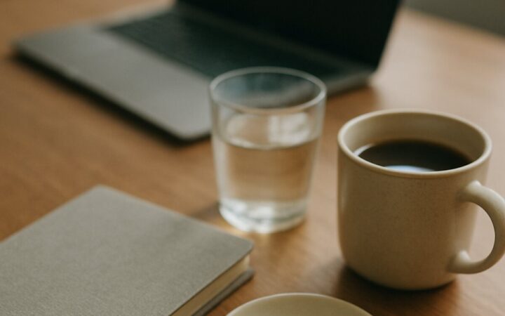A desk with two pale capsules and two dark capsules in a dish beside a laptop and coffee