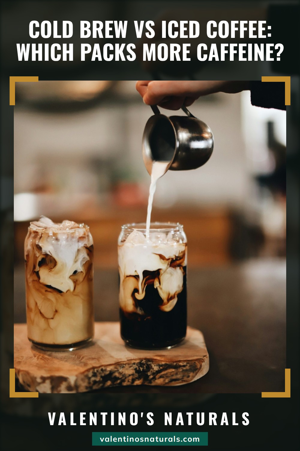 A hand pouring cream into one of two glasses of iced coffee on a wooden board, the other already swirled with milk