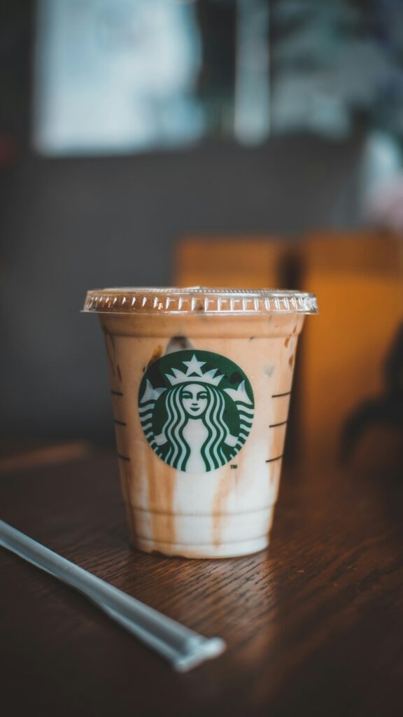 A half-finished iced coffee drink in a clear Starbucks cup with a lid on a wooden cafe table, a wrapped straw beside it