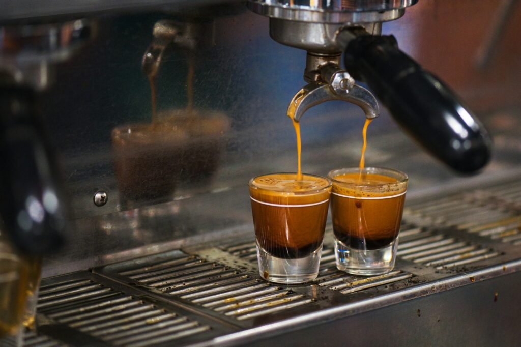 Two espresso shots pouring from a double spout into two small glasses on an espresso machine