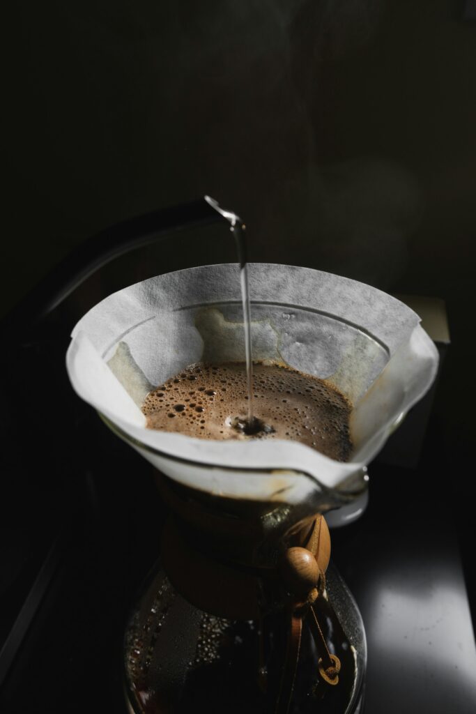 Hot water streaming into a paper filter of blooming coffee grounds in a glass pour-over brewer