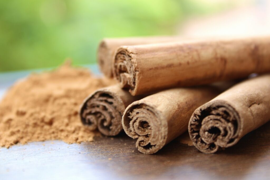 Four cinnamon sticks stacked beside a small pile of ground cinnamon on a dark wooden board
