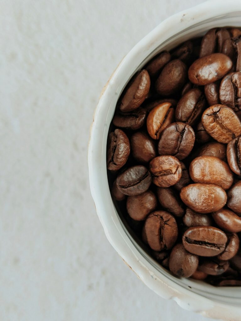 Roasted coffee beans in a white ceramic bowl seen from above on a pale table