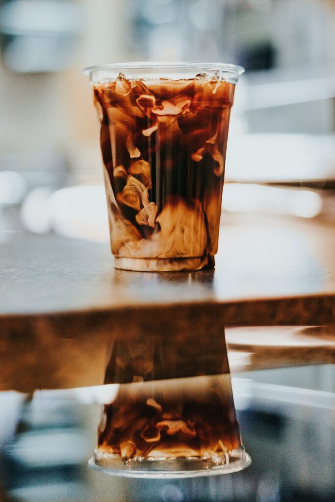 Cold brew with milk swirling through it in a clear cup on a glossy table that mirrors it